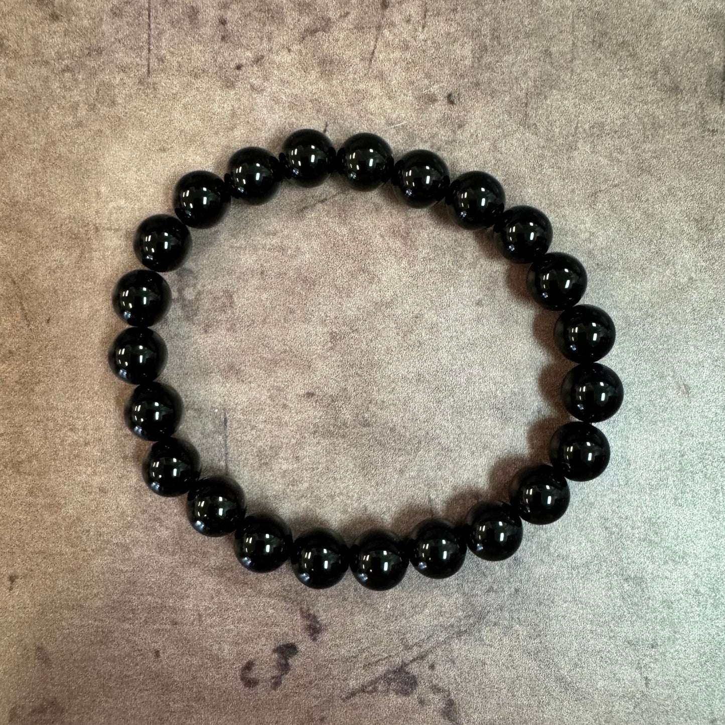 Black beaded bracelet on a textured beige surface