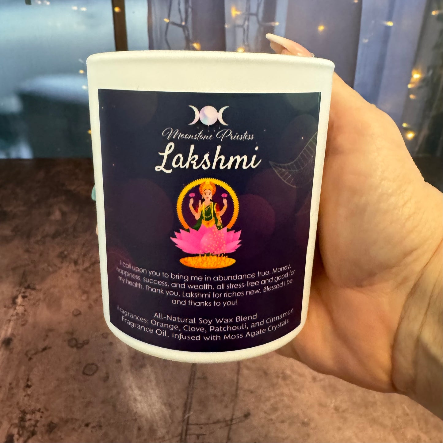 Hand holding a candle labeled 'Lakshmi' with a dark label featuring text and graphics.