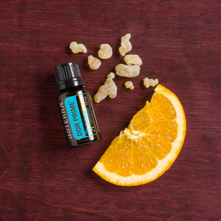 doTERRA Frankincense essential oil bottle with frankincense resin and an orange slice on a dark wooden surface