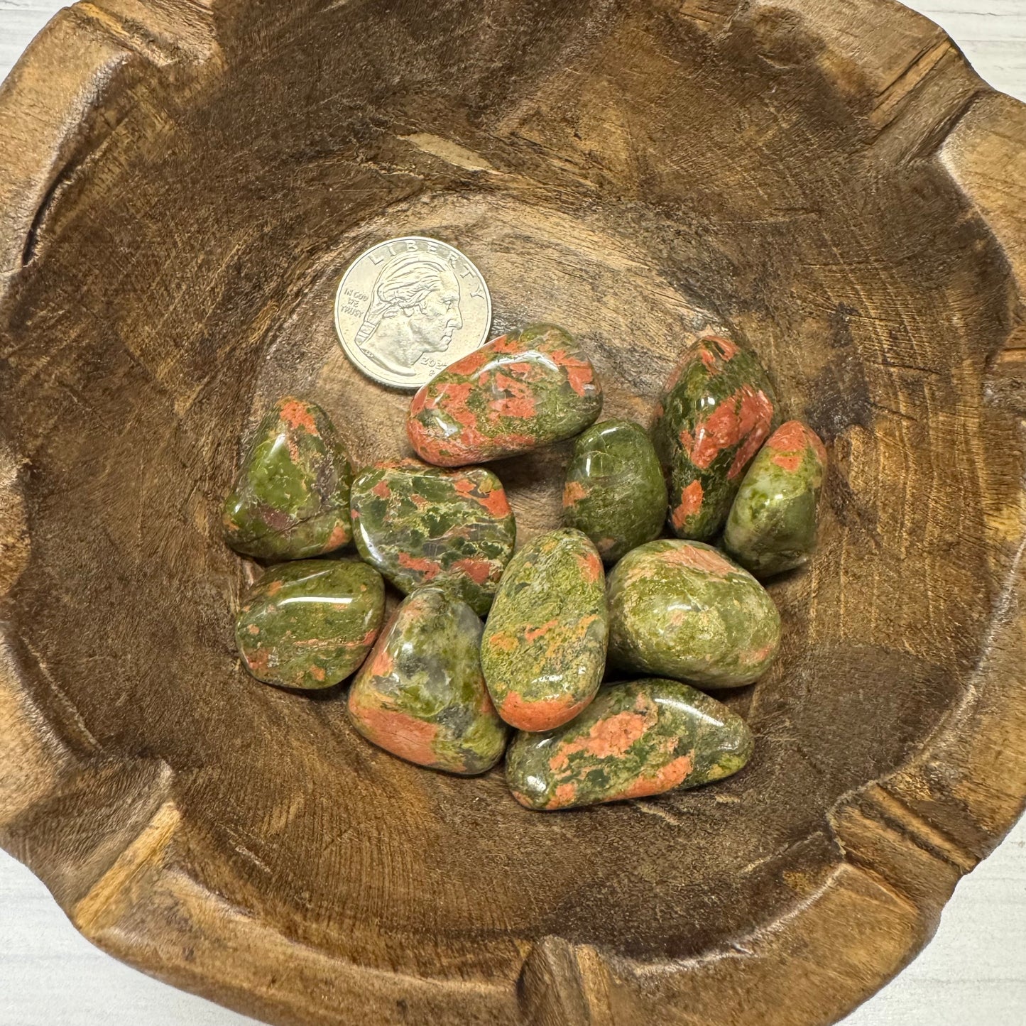 Wooden bowl with green and red stones and a silver coin inside