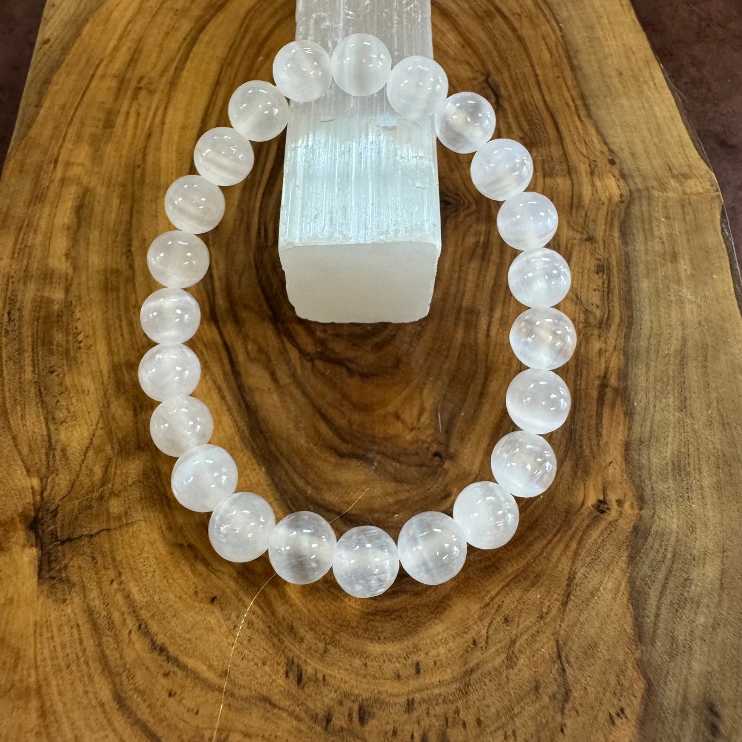 White beaded bracelet on a wooden surface with a crystal in the background