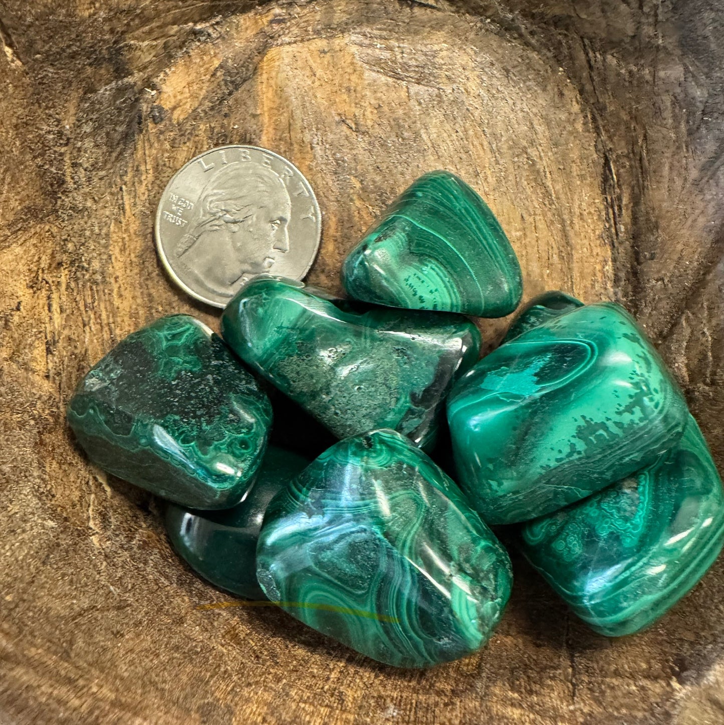 Green malachite stones on a wooden surface with a coin for scale.