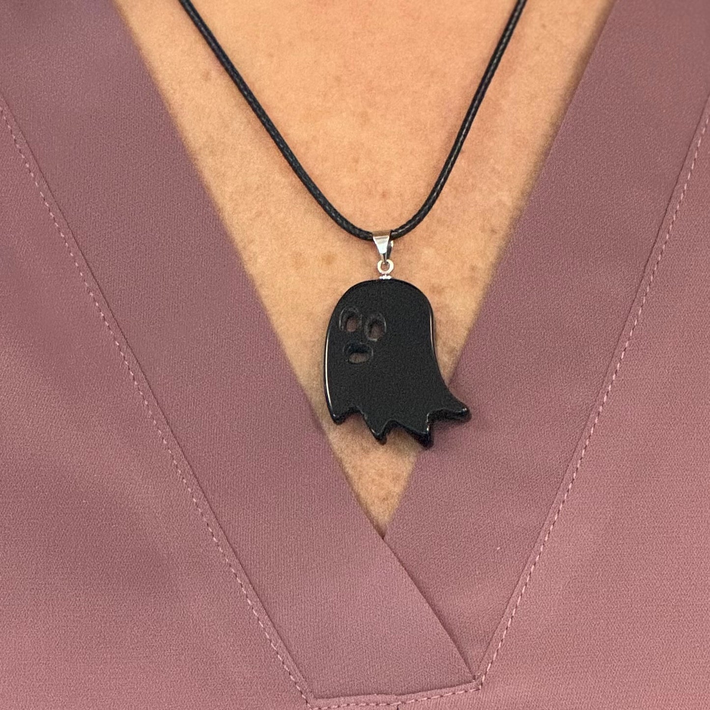 Black ghost-shaped pendant on a black cord against a pink fabric background