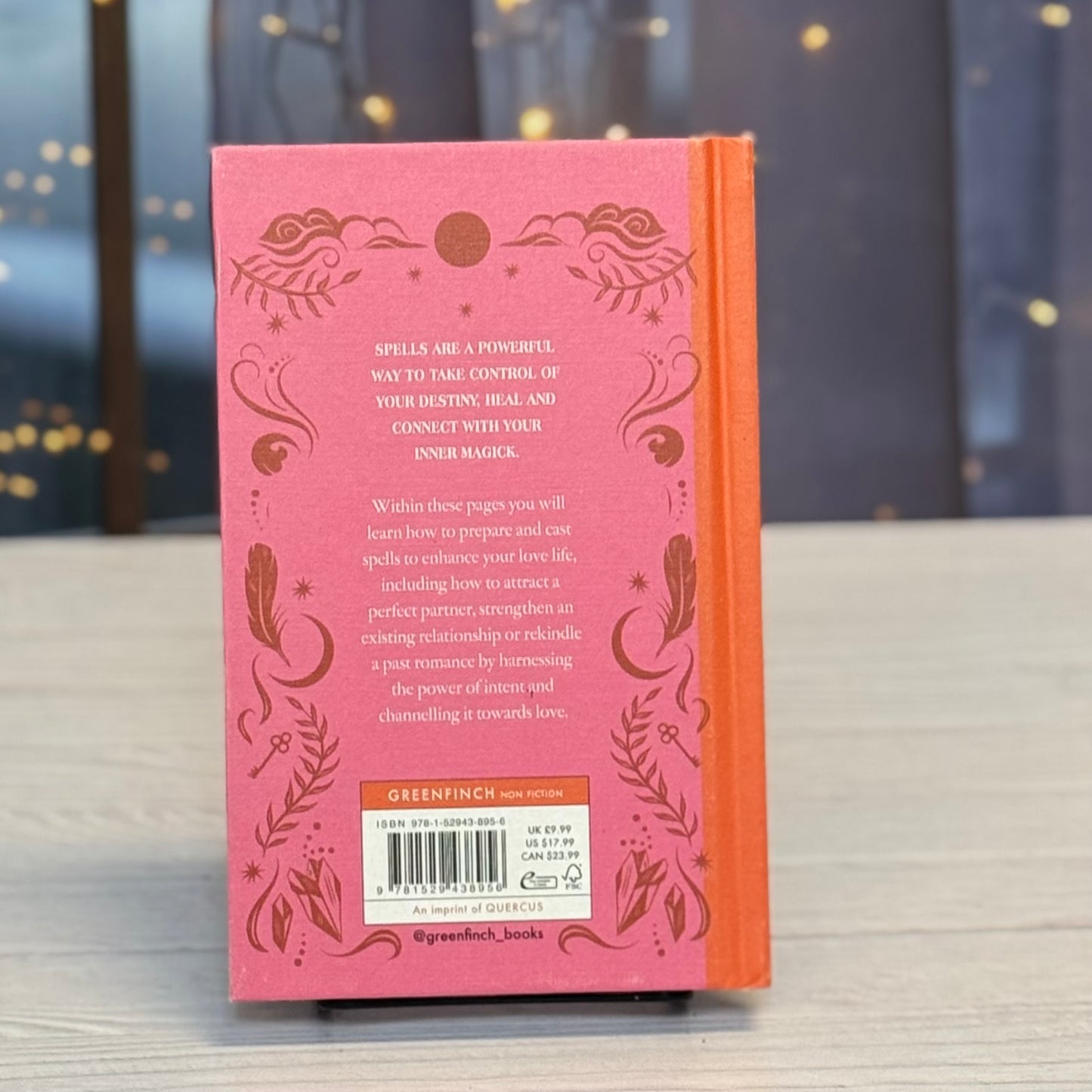 Pink book with decorative text and design on a wooden surface with a blurred background