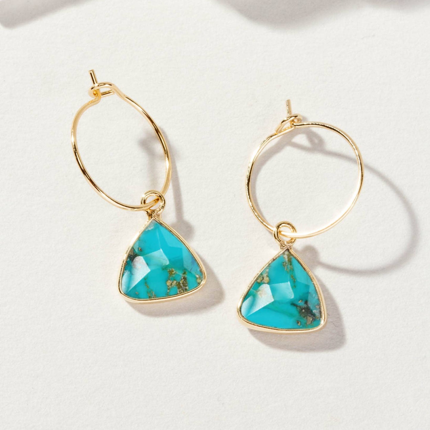 Gold hoop earrings with turquoise triangular stones on a white background