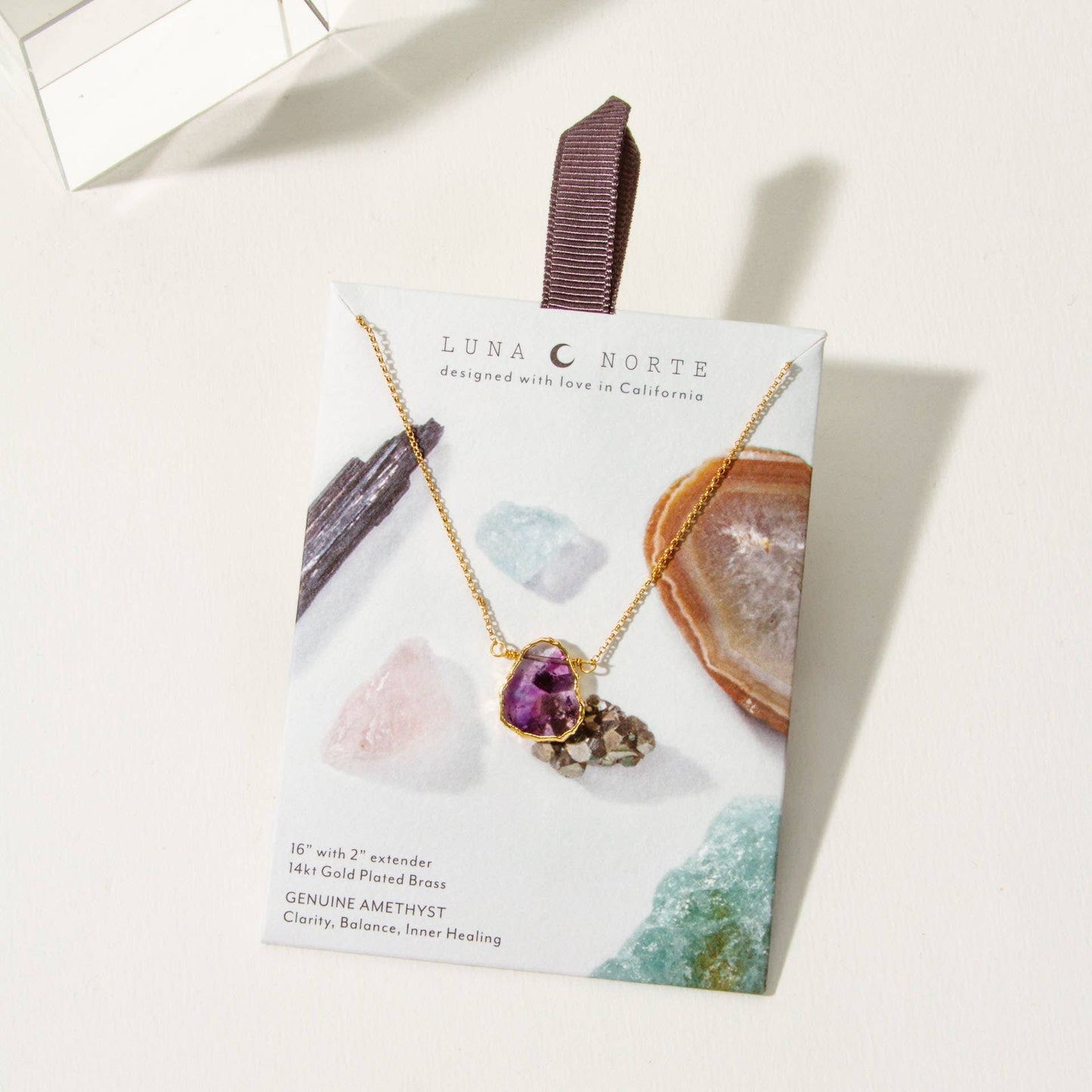 Luna Norte necklace packaging with a gold necklace featuring a purple gemstone on a white background
