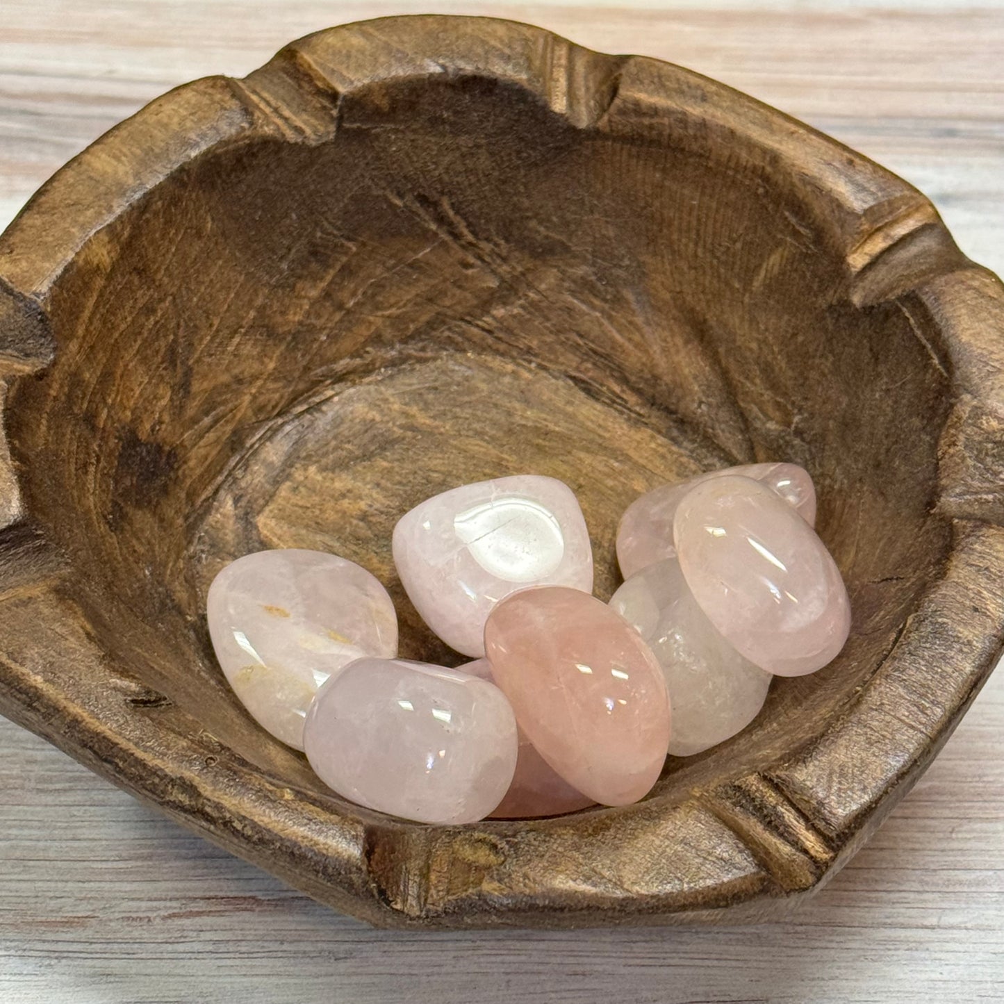 Wooden bowl with rose quartz stones on a light wooden surface