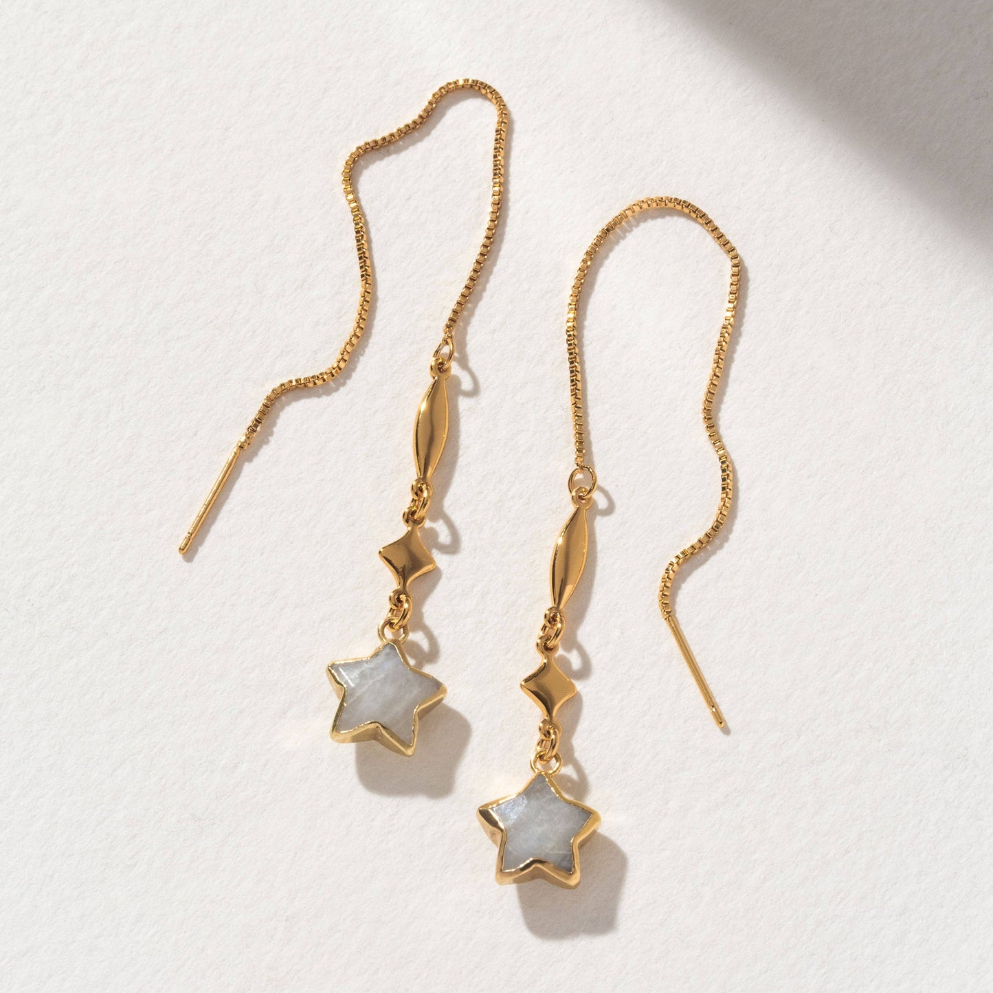 Gold earrings with star-shaped charms on a light background