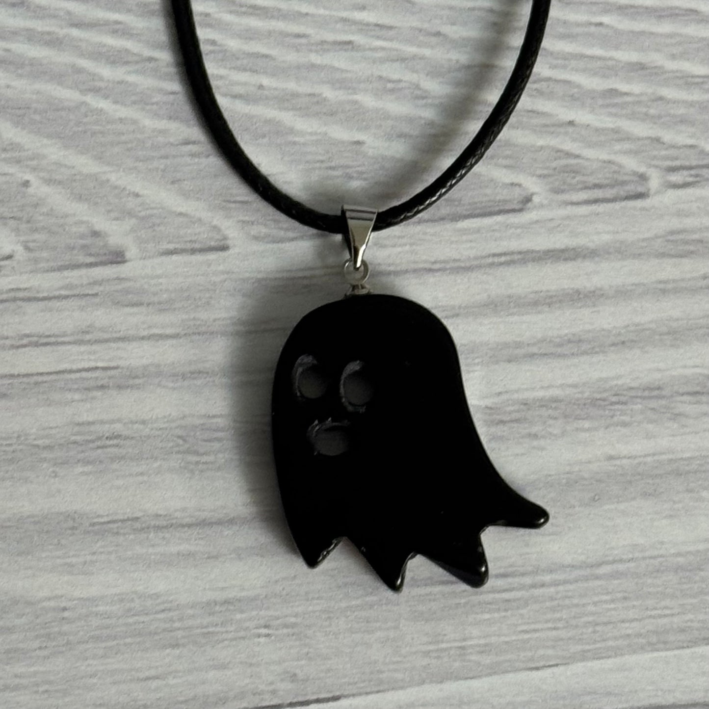 Black ghost-shaped pendant on a black cord against a gray background