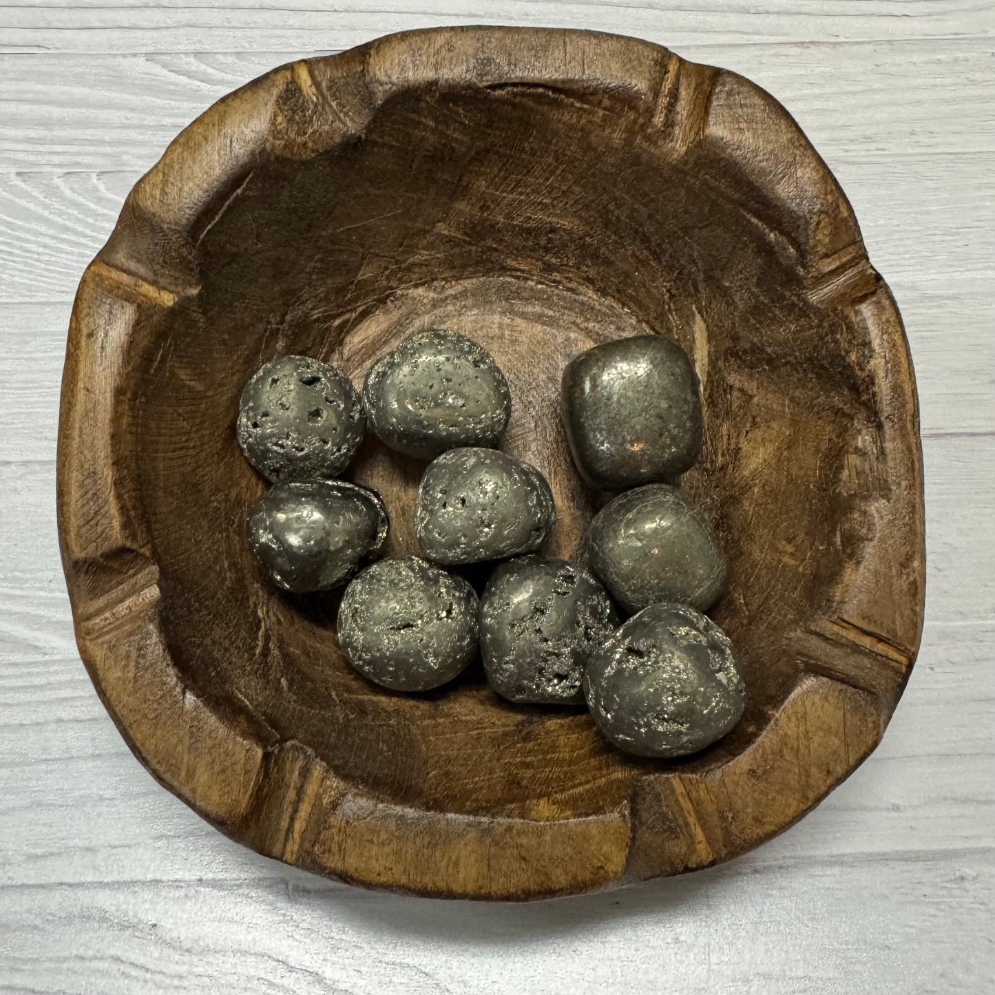Wooden bowl with metallic stones on a light wooden surface