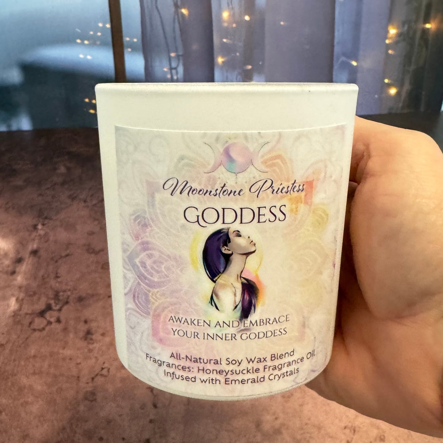 Candle labeled 'Goddess' held by a hand with a blurred background