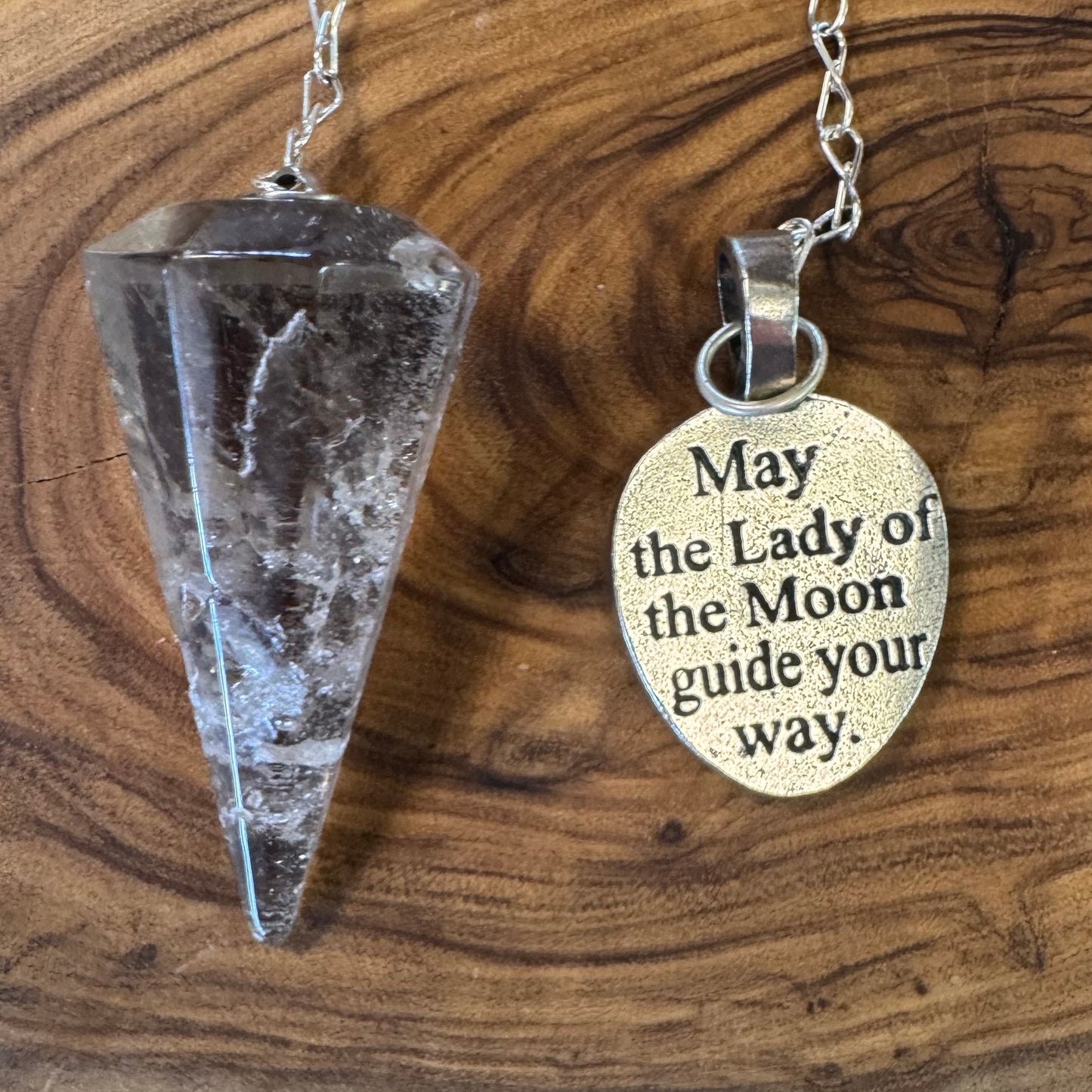 Crystal pendulum and pendant with engraved text on a wooden surface