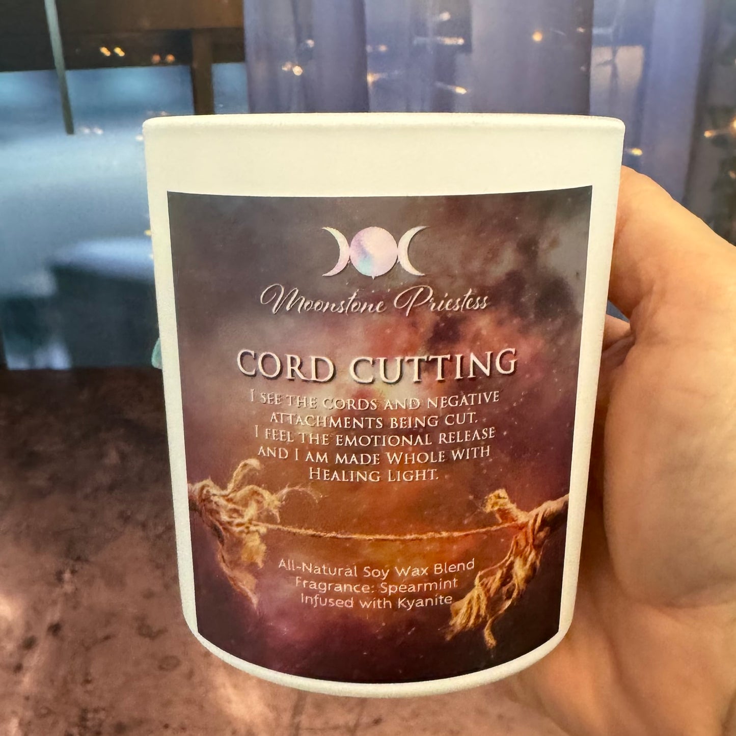Candle with 'Moonstone Priestess' label and 'Cord Cutting' description held by a hand.