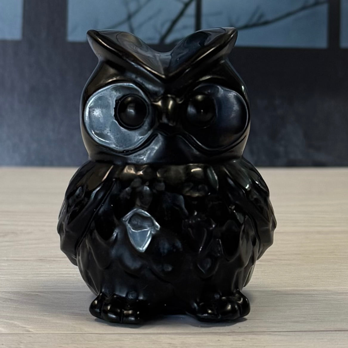 Black owl-shaped decorative item on a wooden surface with a blurred background
