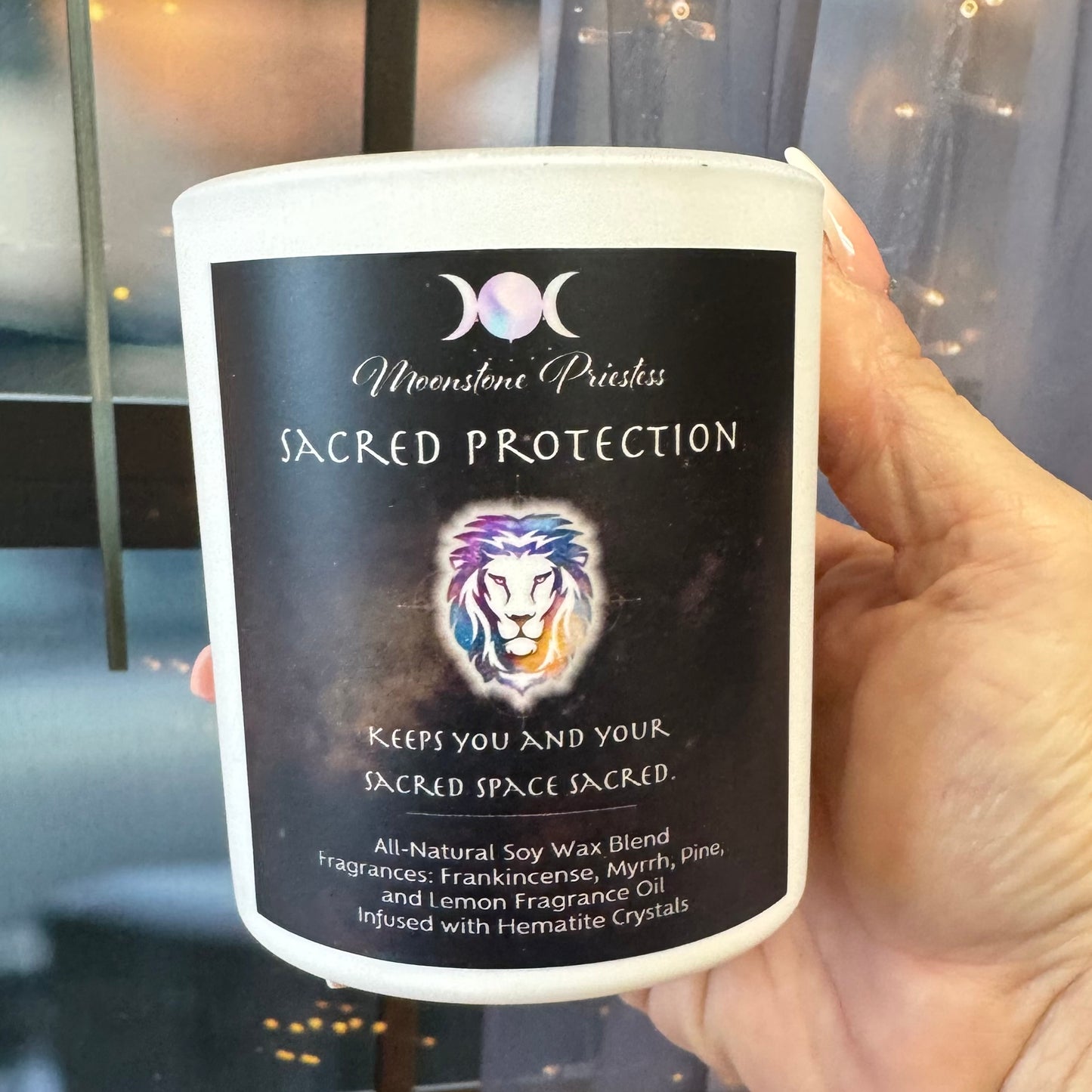 Candle labeled 'Sacred Protection' held by a hand with a blurred background