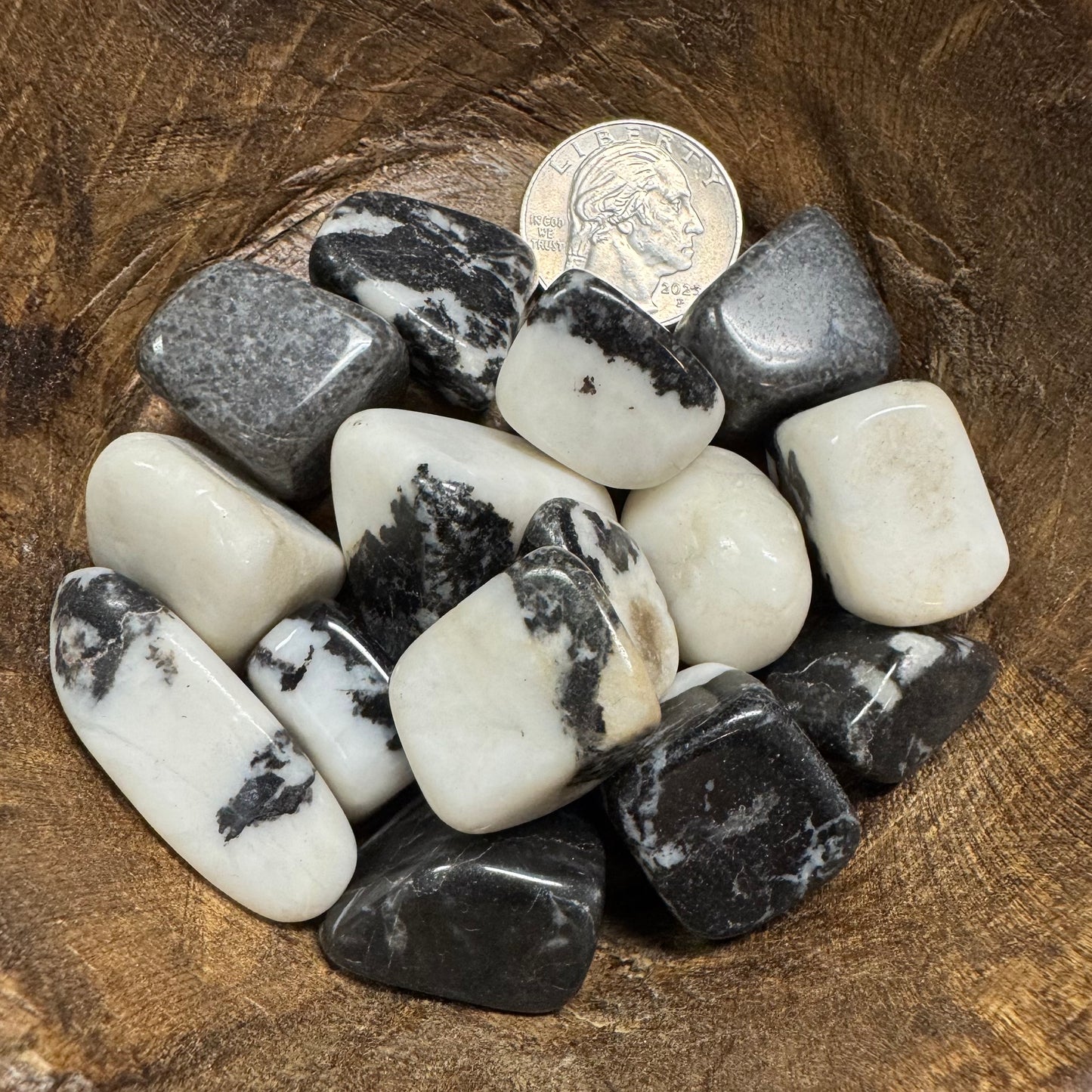 Collection of black and white stones on a wooden surface with a coin for scale.