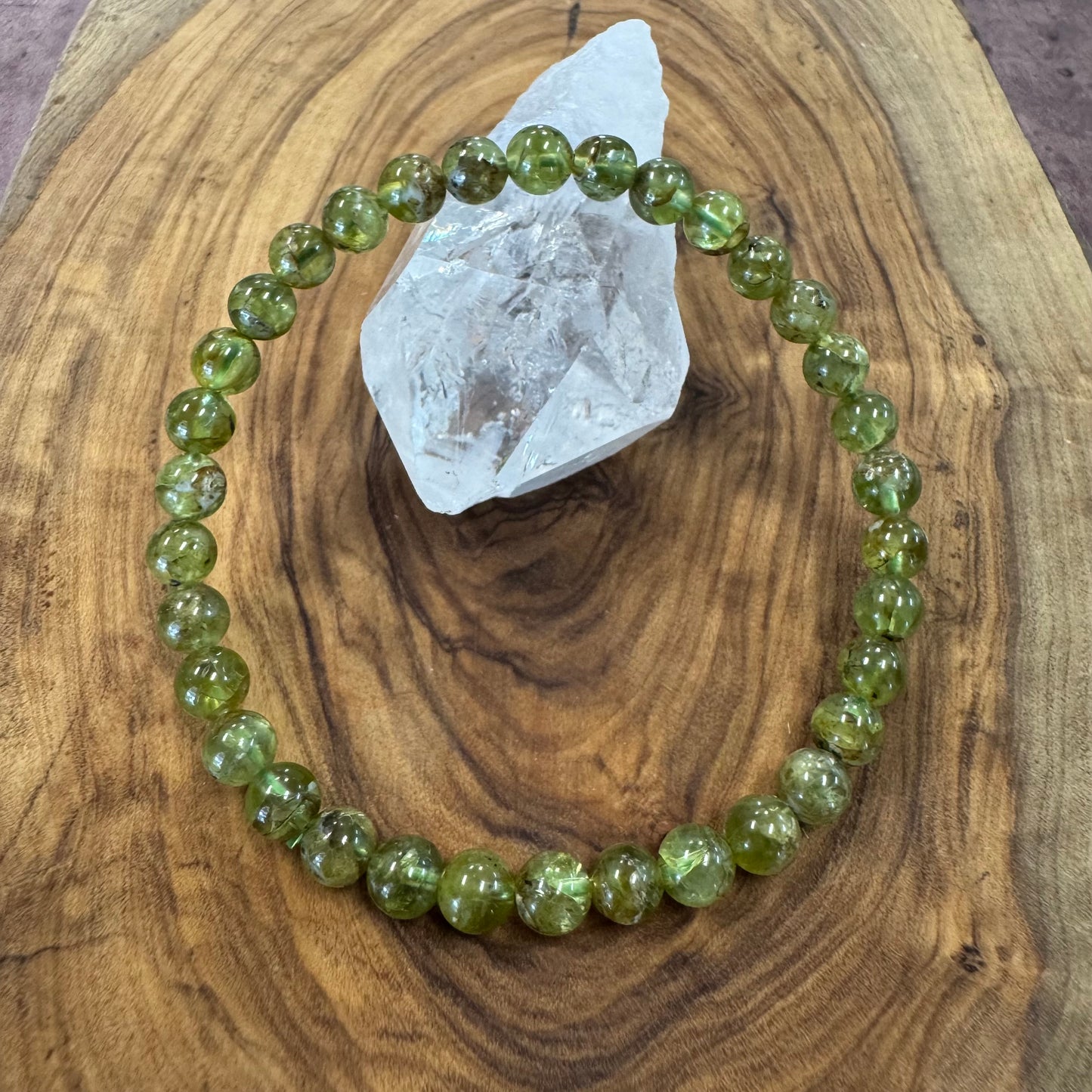 Green beaded bracelet on a wooden surface with a crystal