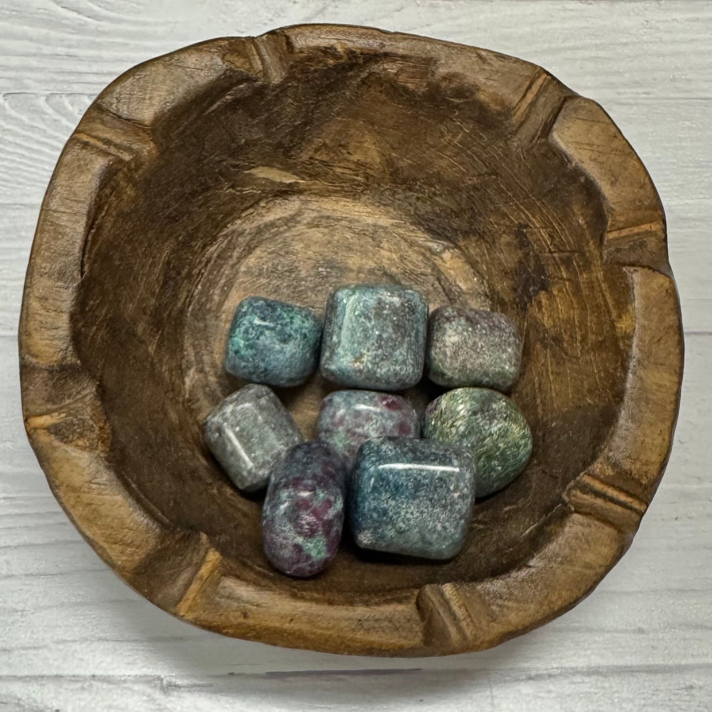 Wooden bowl with colorful stones on a light wooden surface
