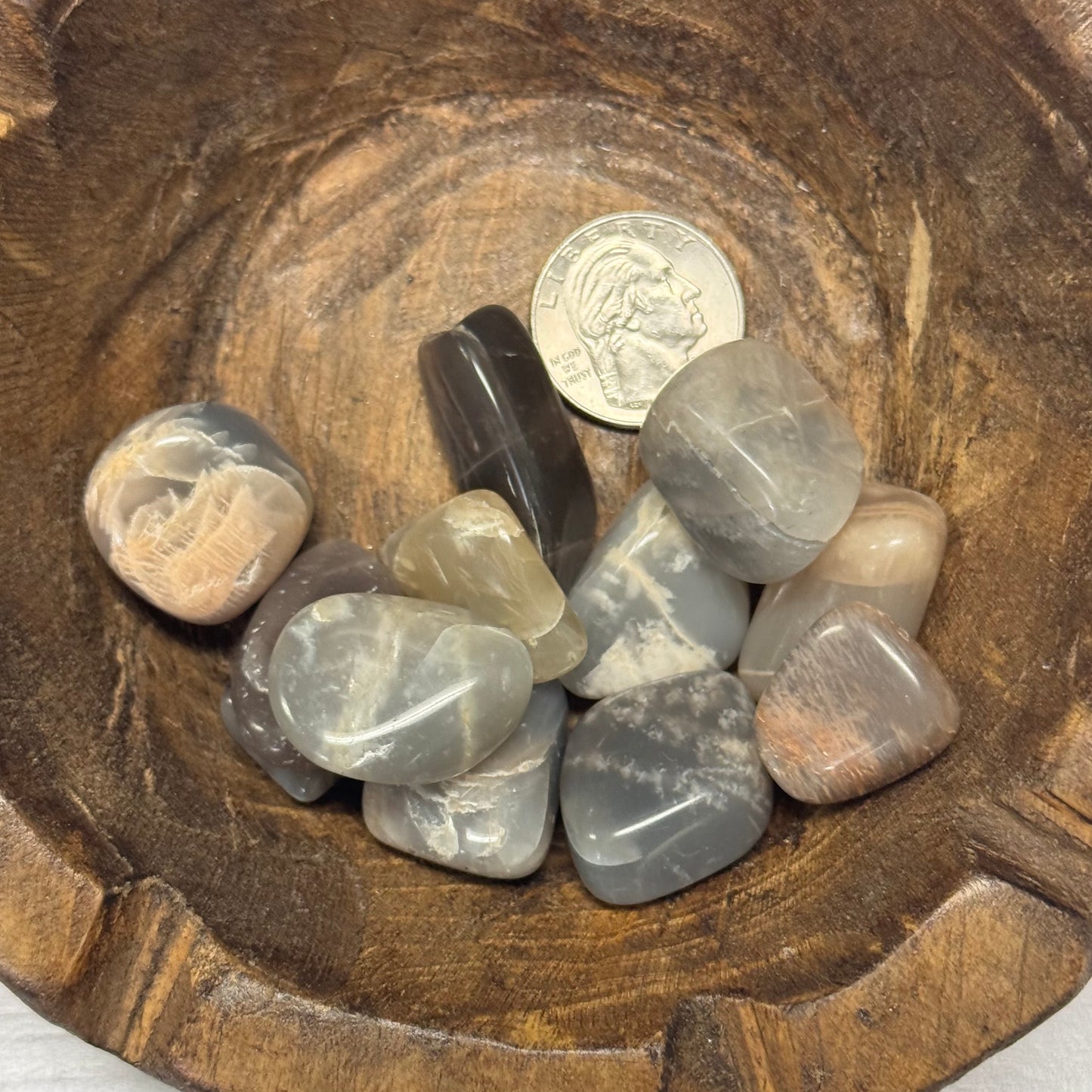 Collection of tumbled stones in a wooden bowl with a quarter for scale.