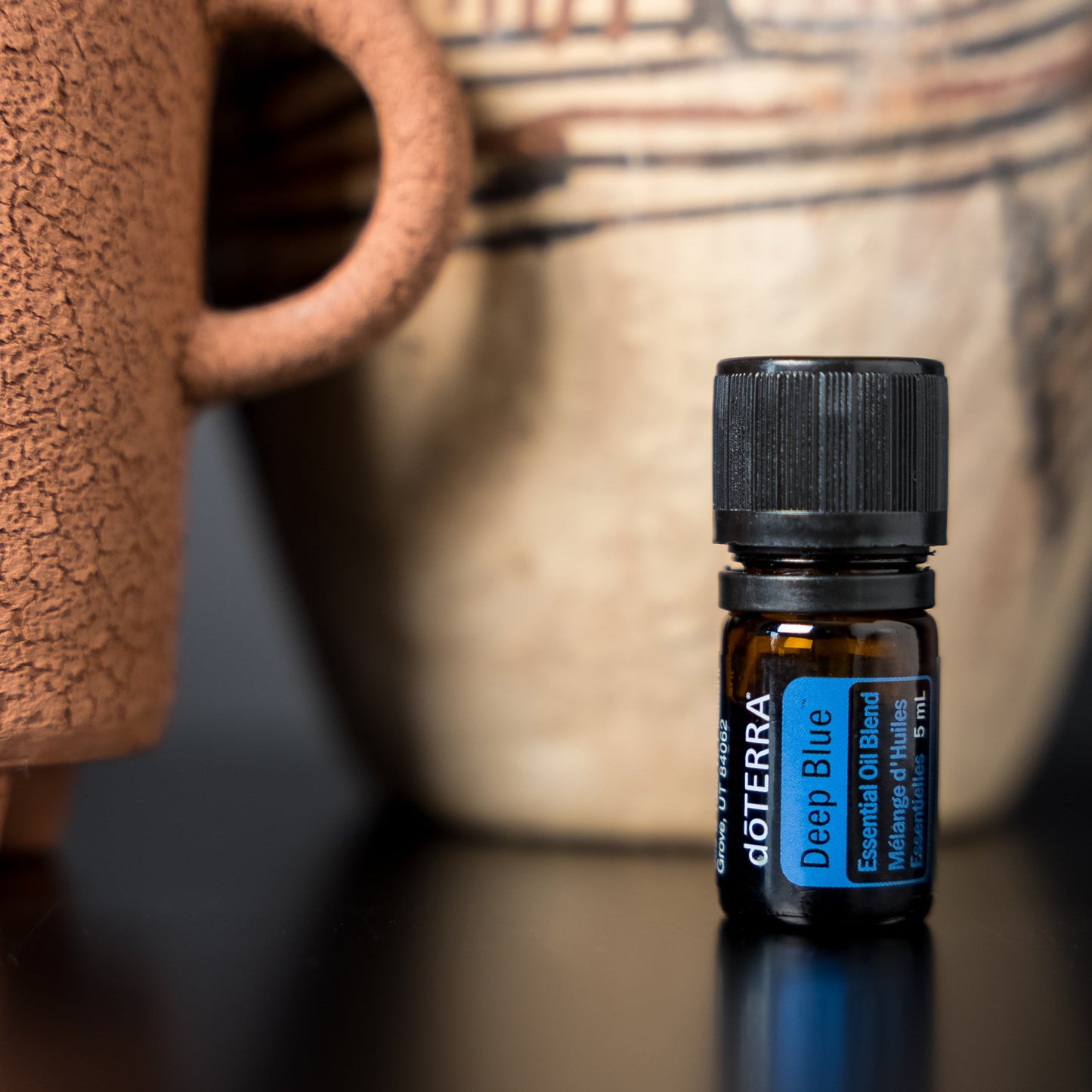 Doterra essential oil bottle on a dark surface with a ceramic mug and vase in the background