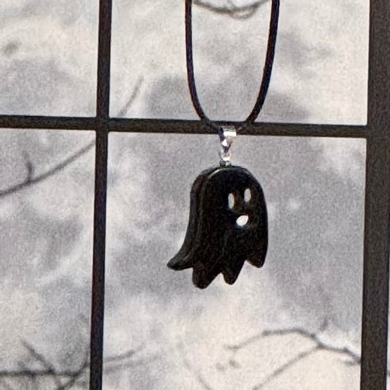 Black ghost-shaped pendant on a cord against a window with a snowy background
