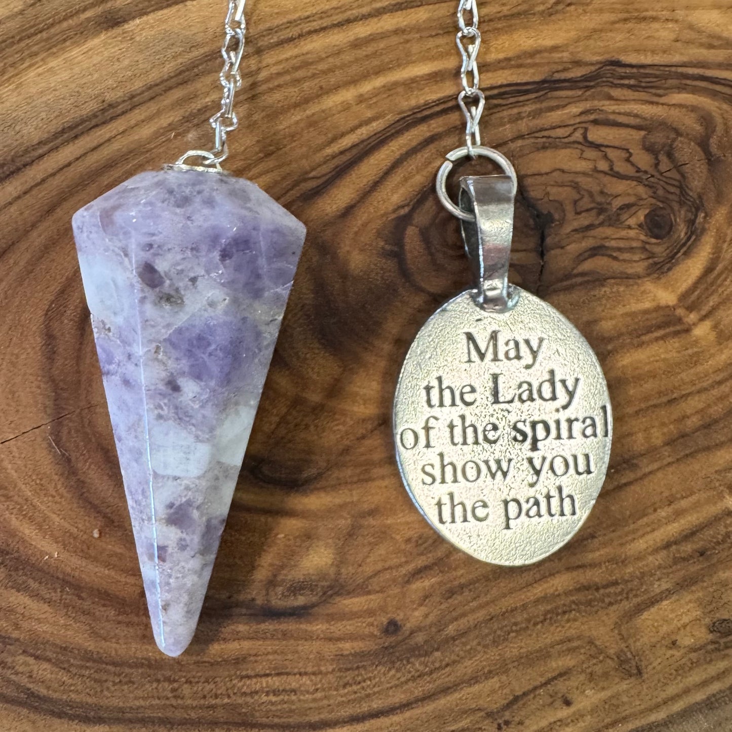 Lepidolite pendulum and silver pendant with engraved text on a wooden surface