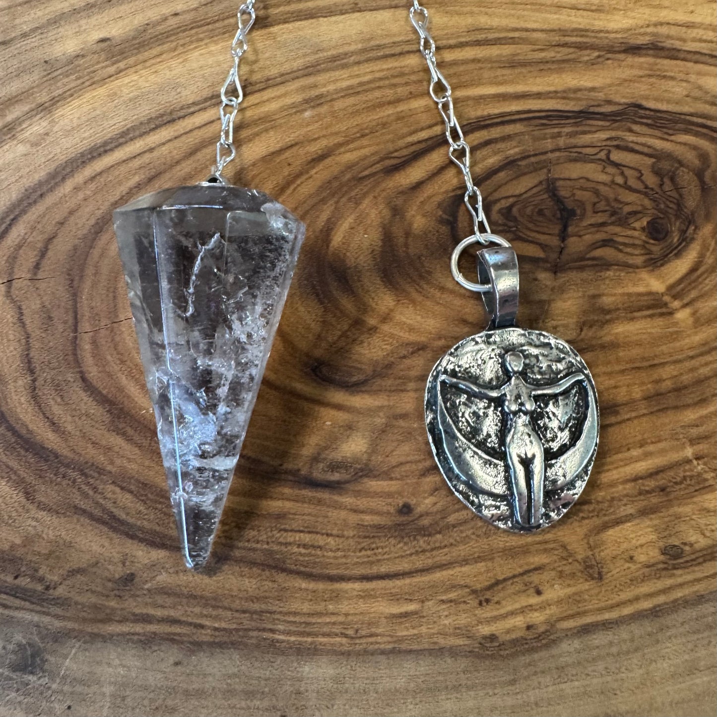 Crystal pendulum and silver pendant on a wooden surface