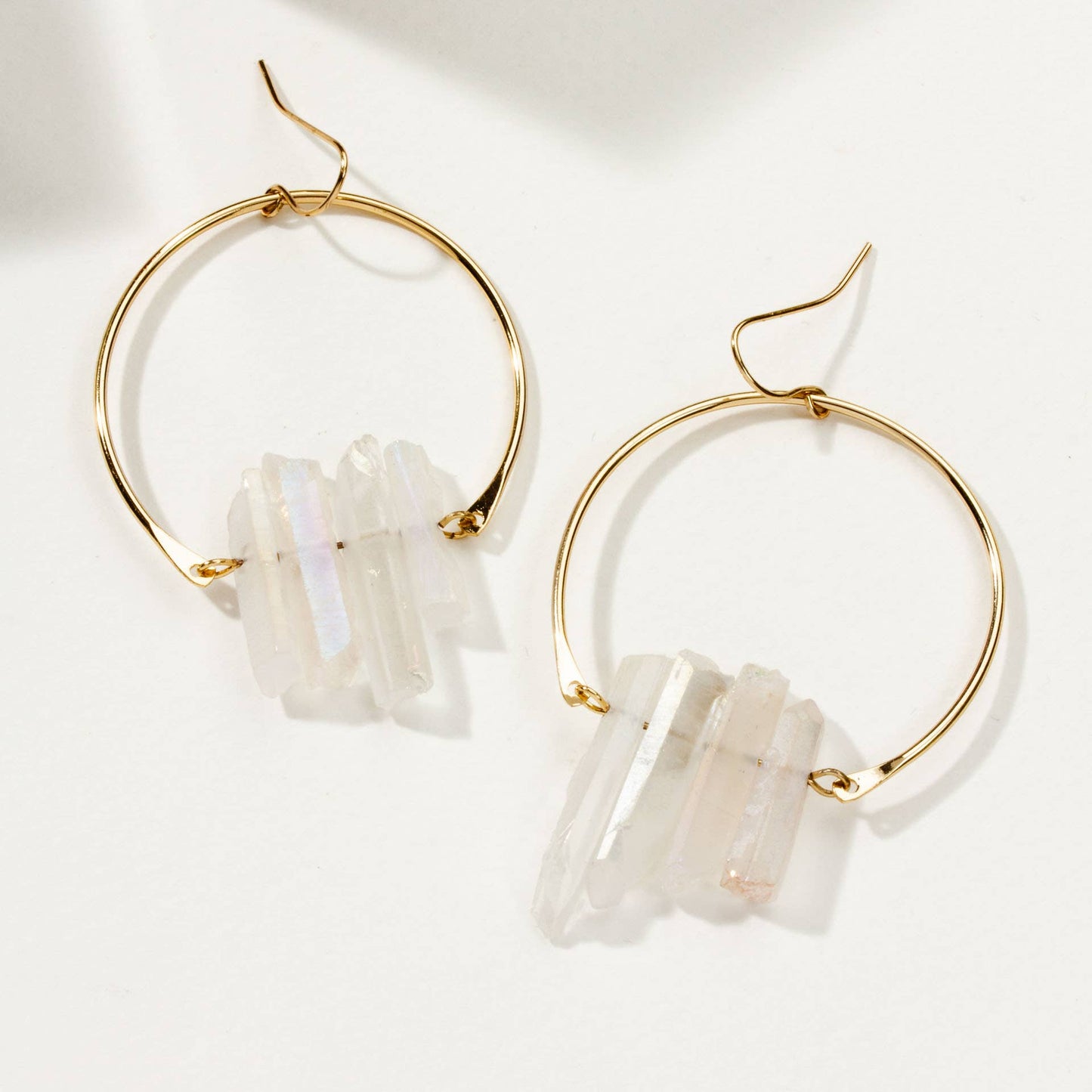 Gold hoop earrings with white stone accents on a light background