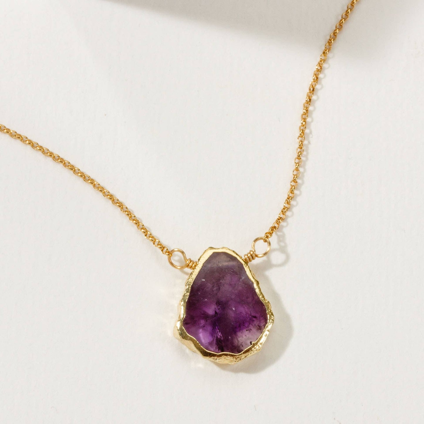 Gold necklace with a purple gemstone pendant on a white background