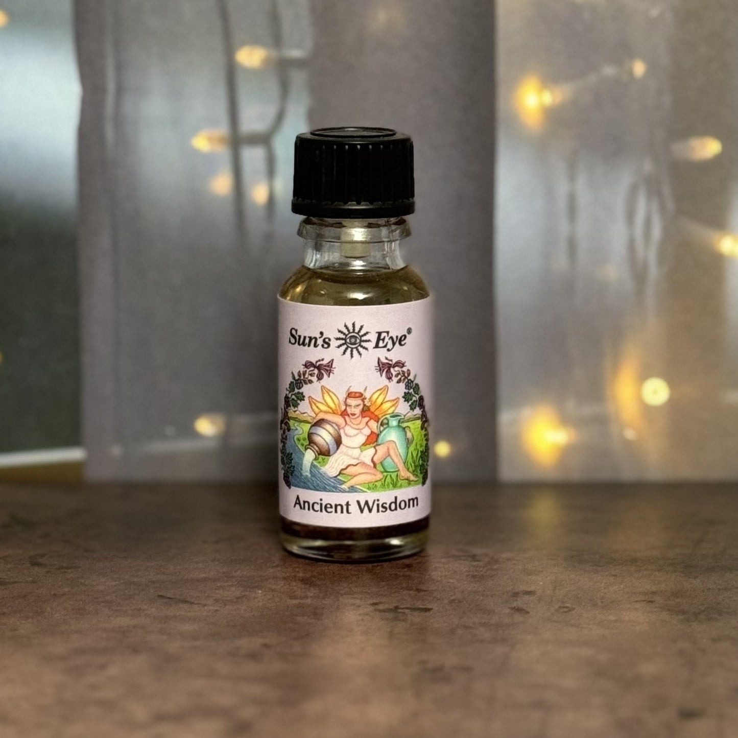 Small bottle labeled 'Sun's Eye Ancient Wisdom' on a reflective surface with blurred lights in the background