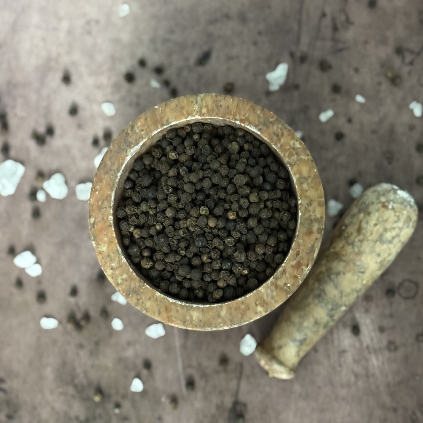 Brass container filled with small black peppercorn on a textured surface