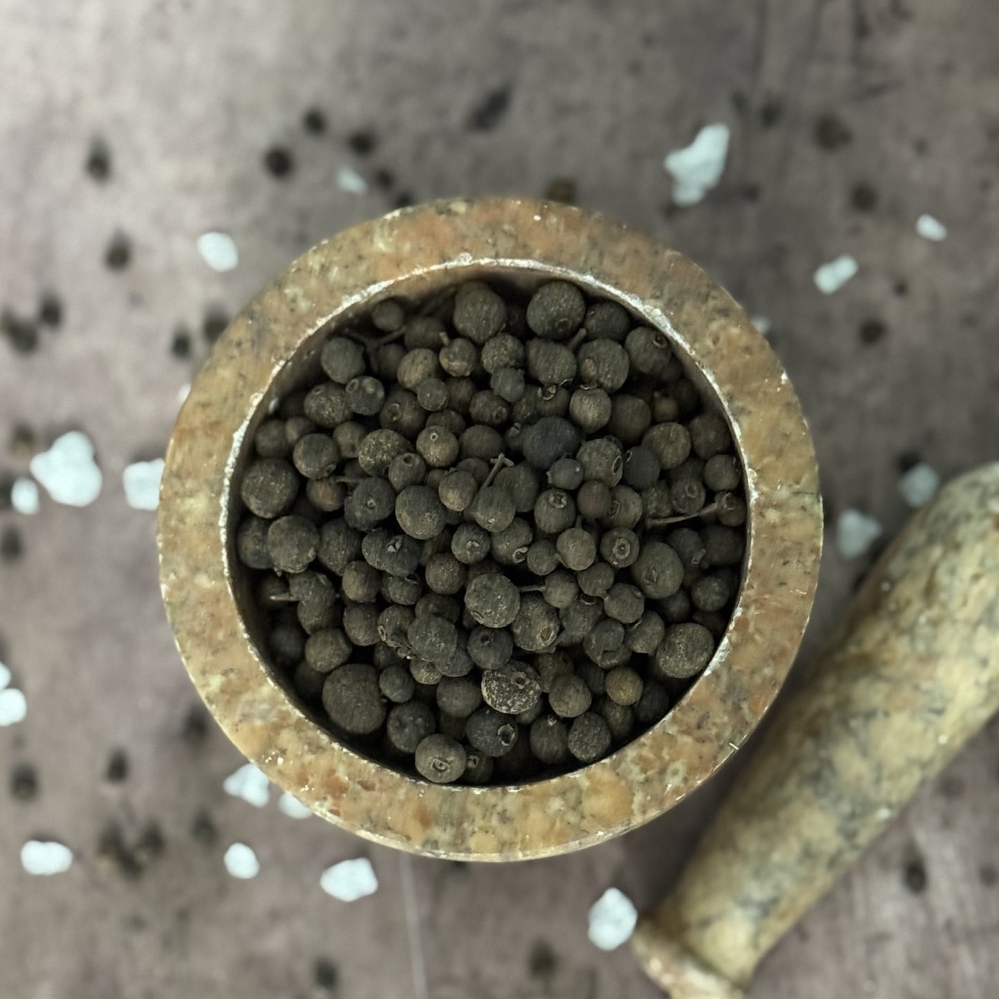 Close-up of a brass tube filled with small allspice on a textured surface.