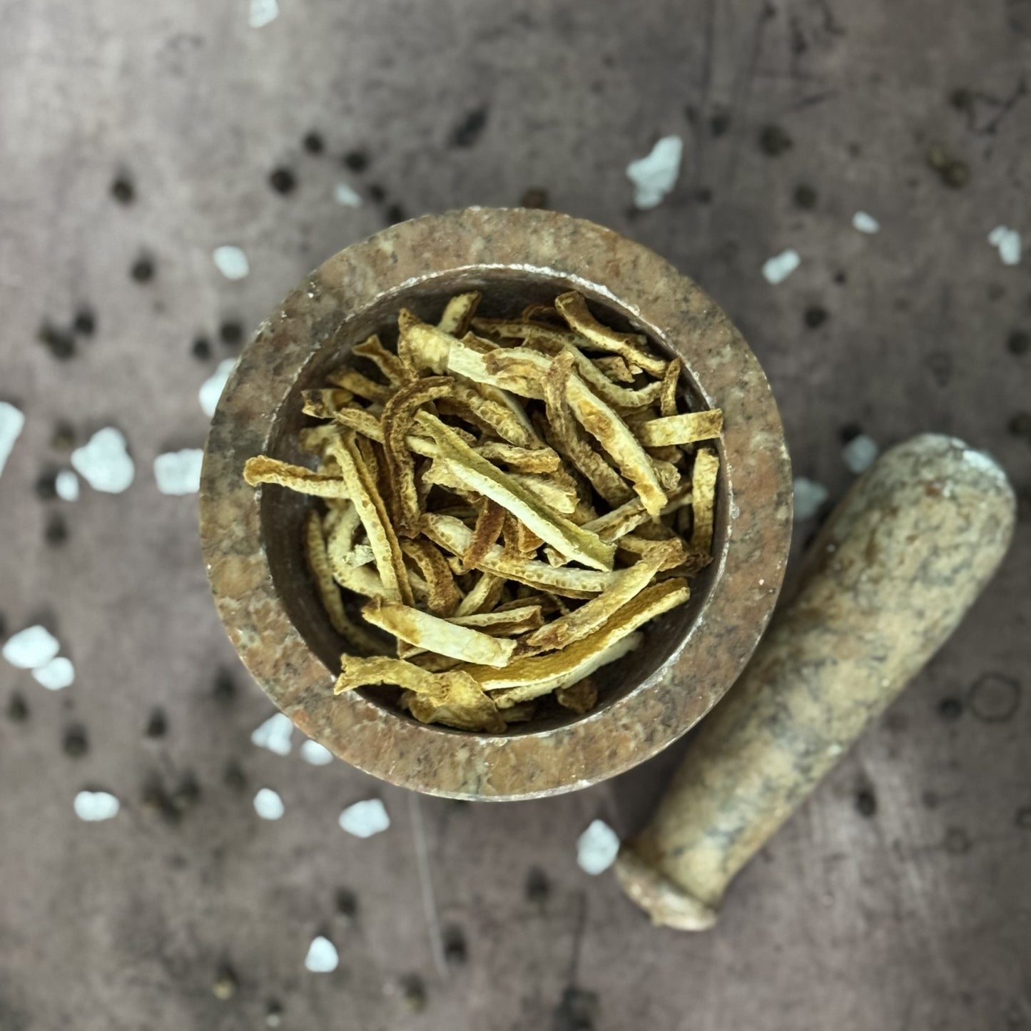 Mortar and pestle with dried orange peels on a textured surface