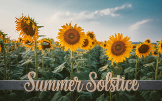 A field of golden sunflowers in full bloom under a soft blue sky, with "Summer Solstice" in wooden cursive lettering across the bottom.