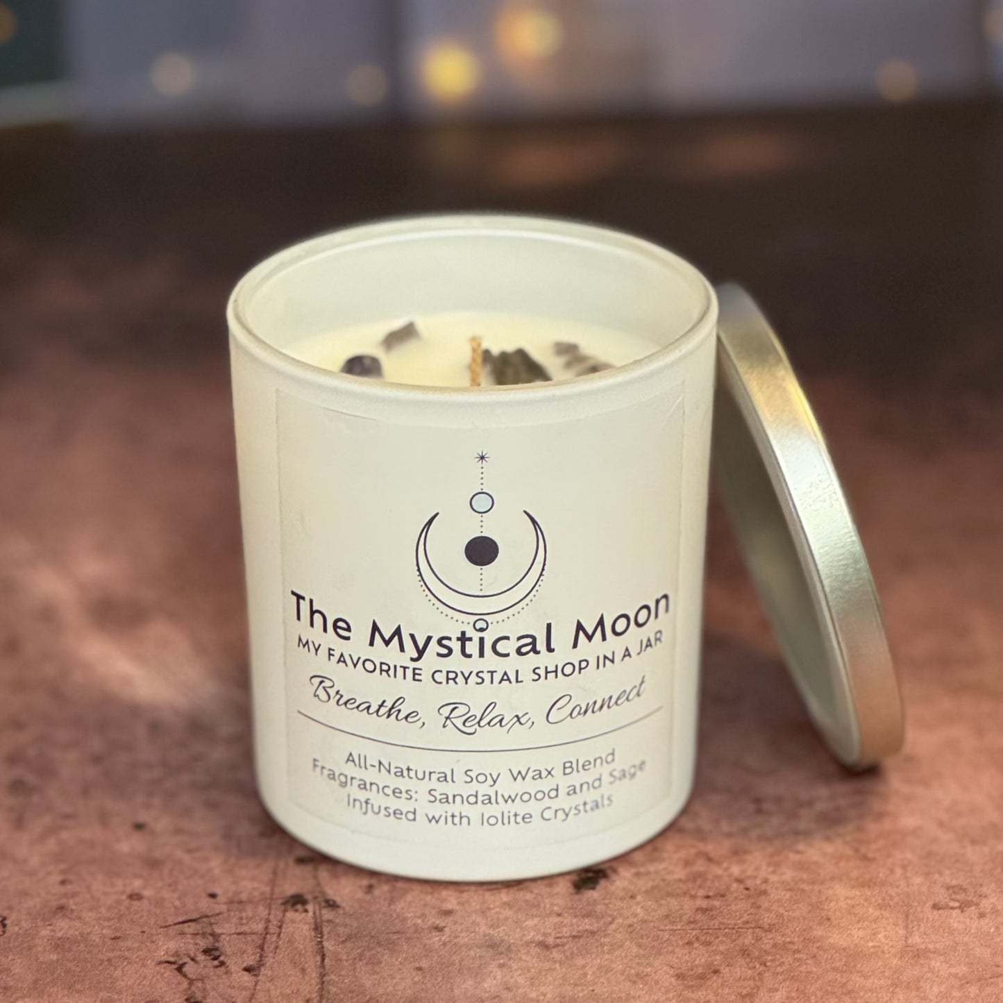 Candle in a white container with 'The Mystical Moon' branding on a wooden surface.