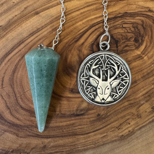 Green aventurine pendulume , one green and one silver with deer design, on a wooden surface.