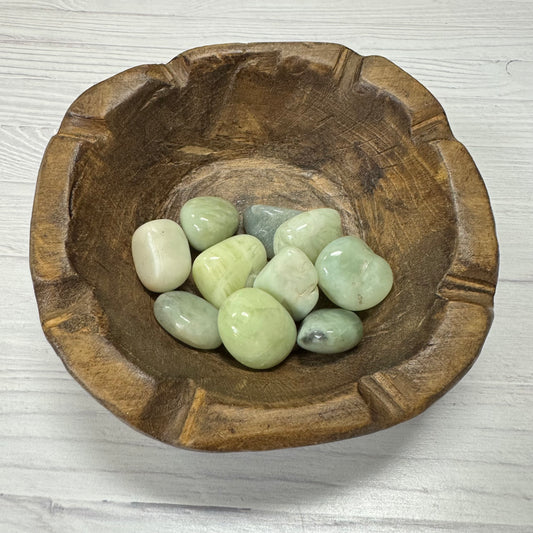 Wooden bowl with green stones on a light wooden surface