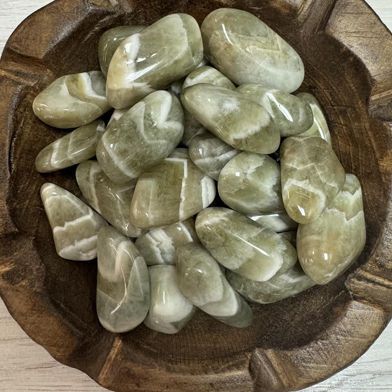 Green stones in a wooden bowl on a light wooden surface