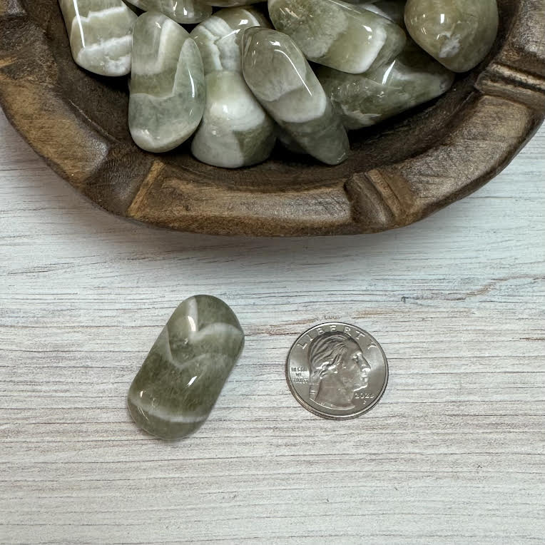 Green stone next to a quarter on a light wooden surface