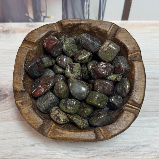 Wooden bowl filled with polished multicolored stones on a light wooden surface.