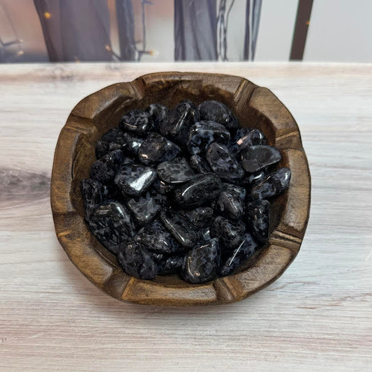 Wooden bowl filled with black stones on a light wooden surface