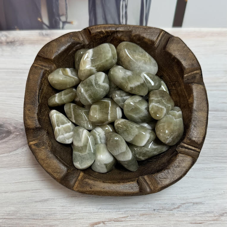 Wooden bowl filled with green stones on a light wooden surface