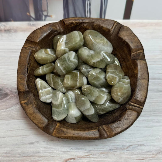 Wooden bowl filled with green stones on a light wooden surface