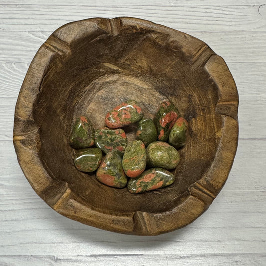 Wooden bowl with green and red stones on a light wooden surface