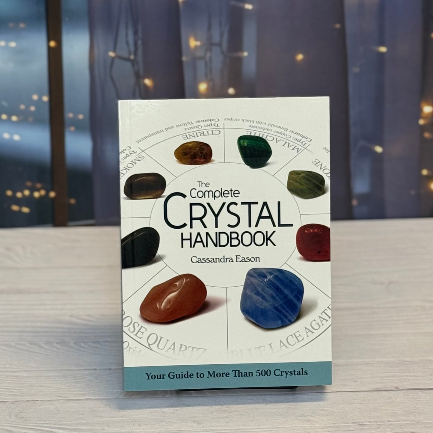 Book titled 'The Complete Crystal Handbook' by Cassandra Eason with crystal images on a blurred nature background.
