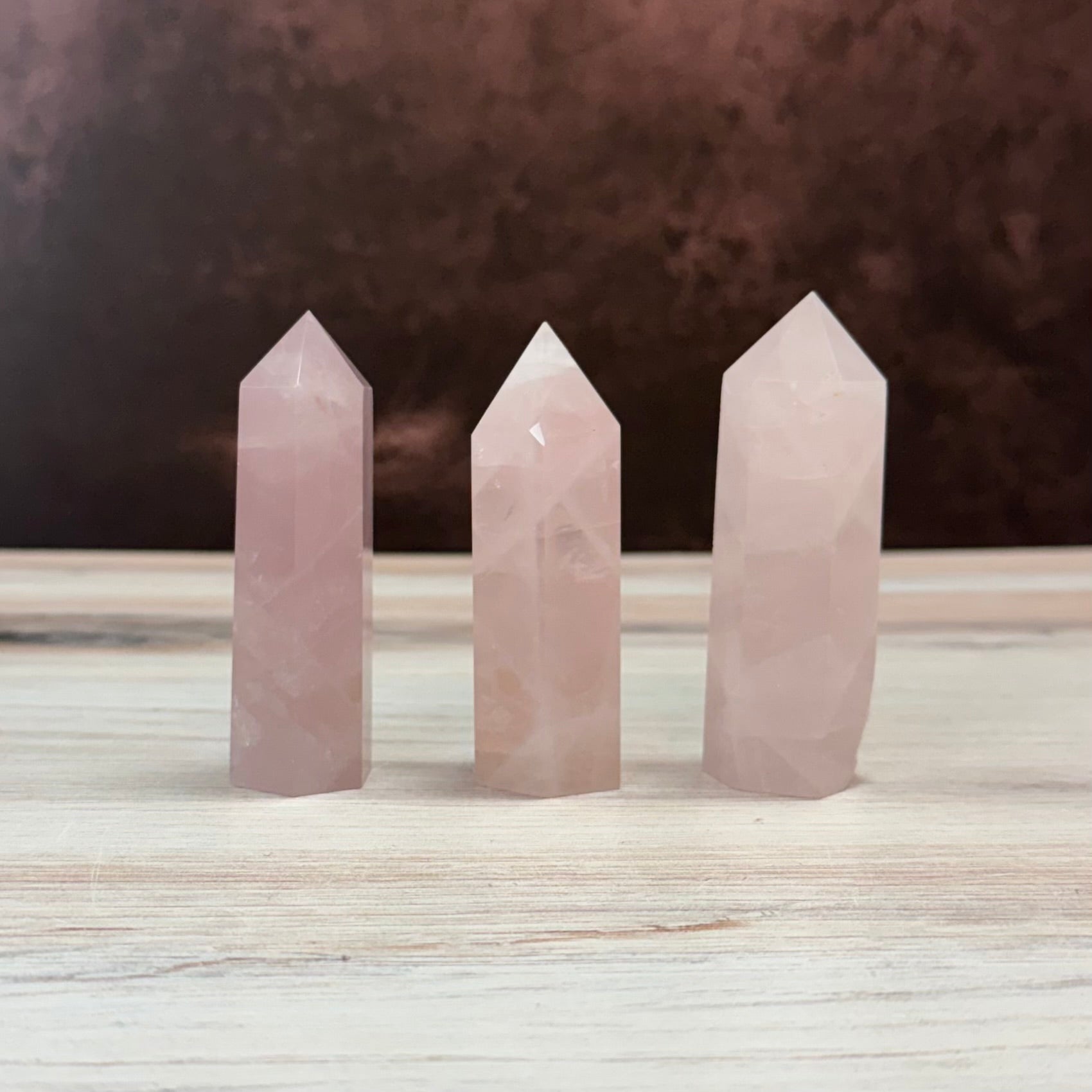 Three rose quartz crystal points on a wooden surface with a dark background