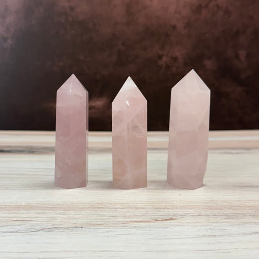 Three rose quartz crystal points on a wooden surface with a dark background