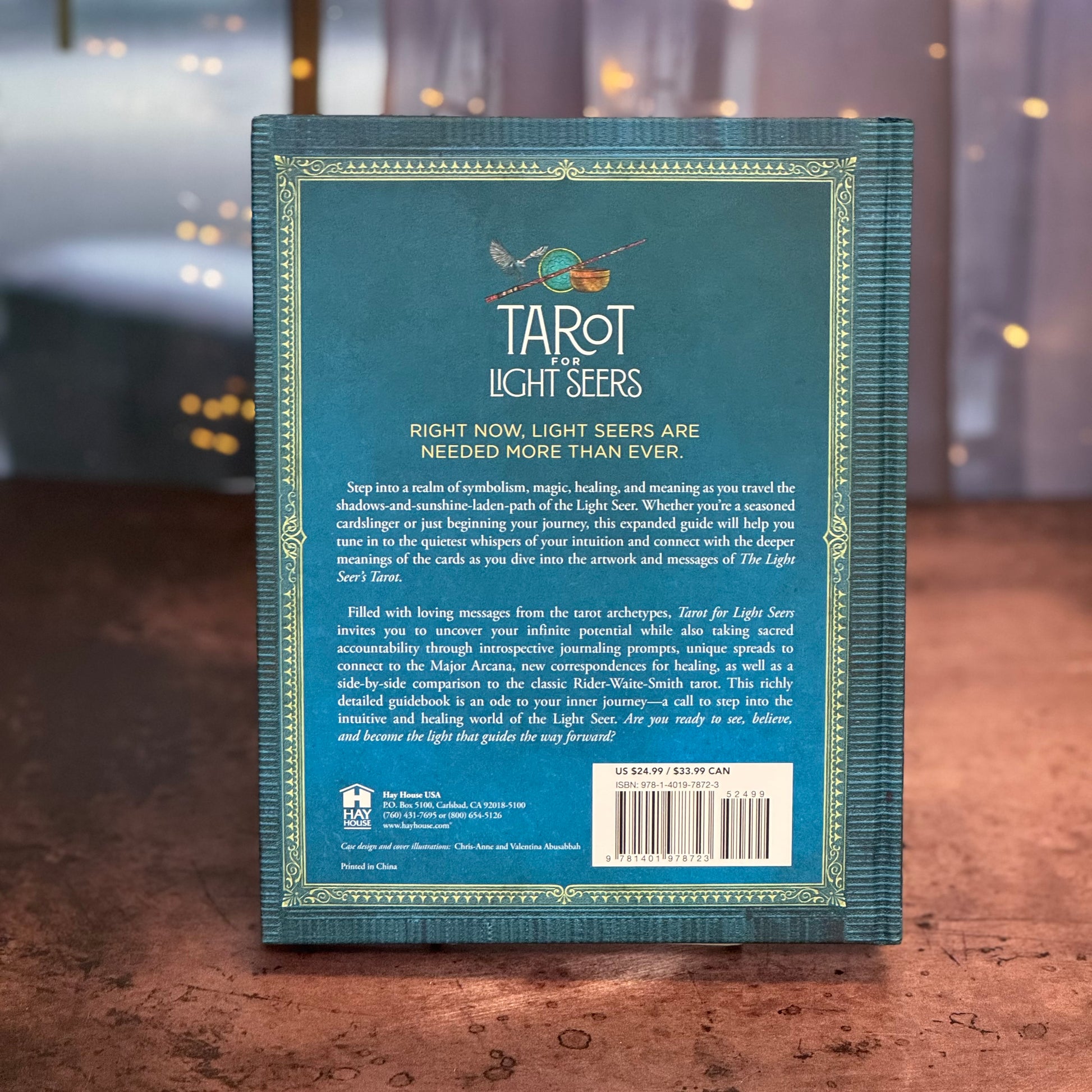 Back cover of a book titled 'Tarot of the Light Seers' on a wooden surface with a blurred background.