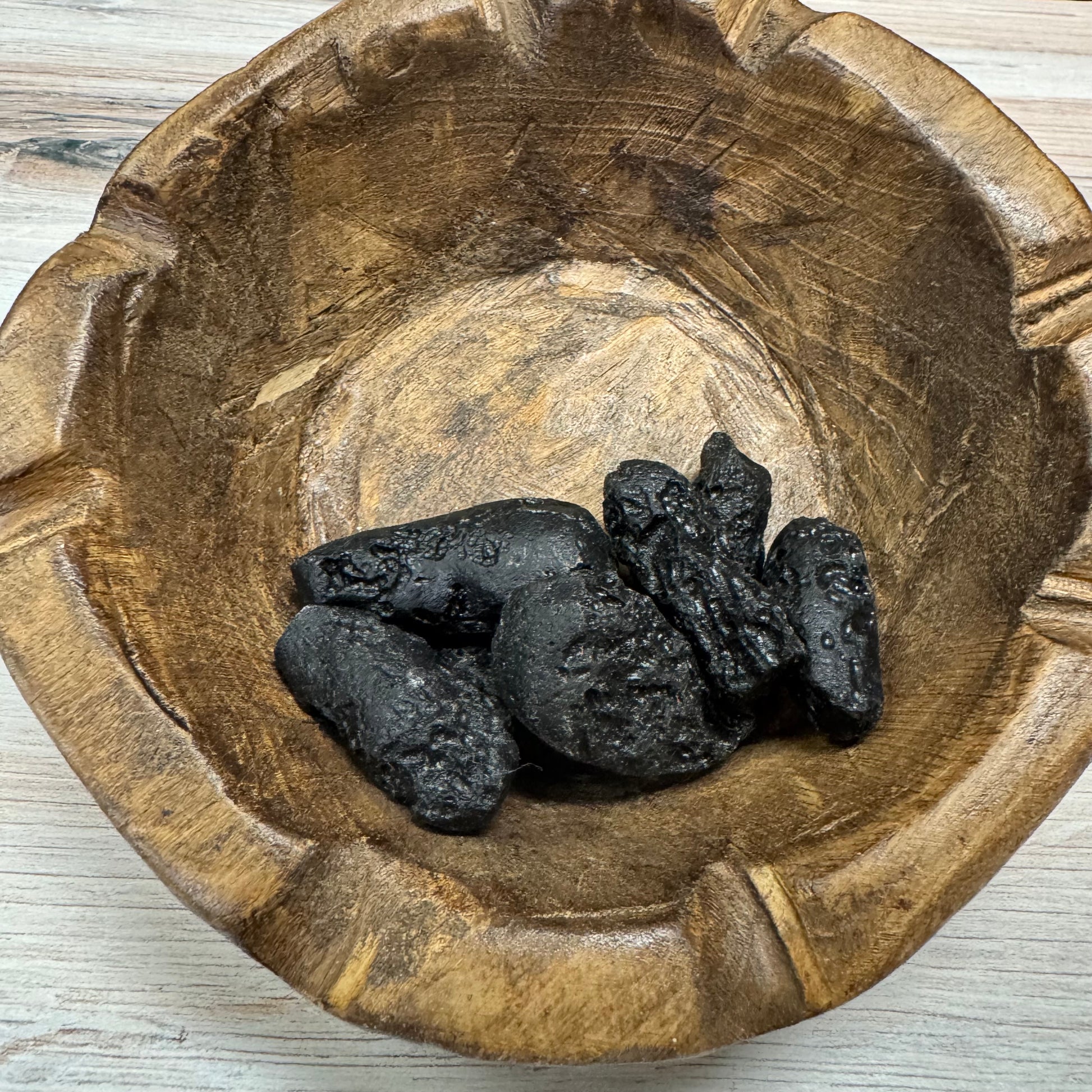 Wooden bowl with tektite on a light wooden surface