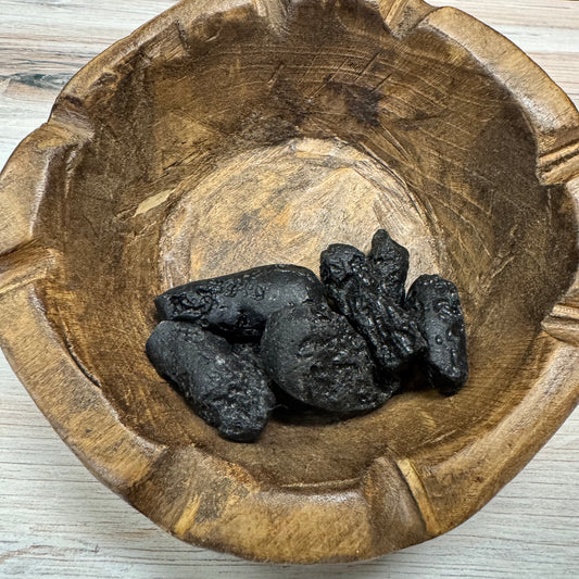 Wooden bowl with tektite on a light wooden surface